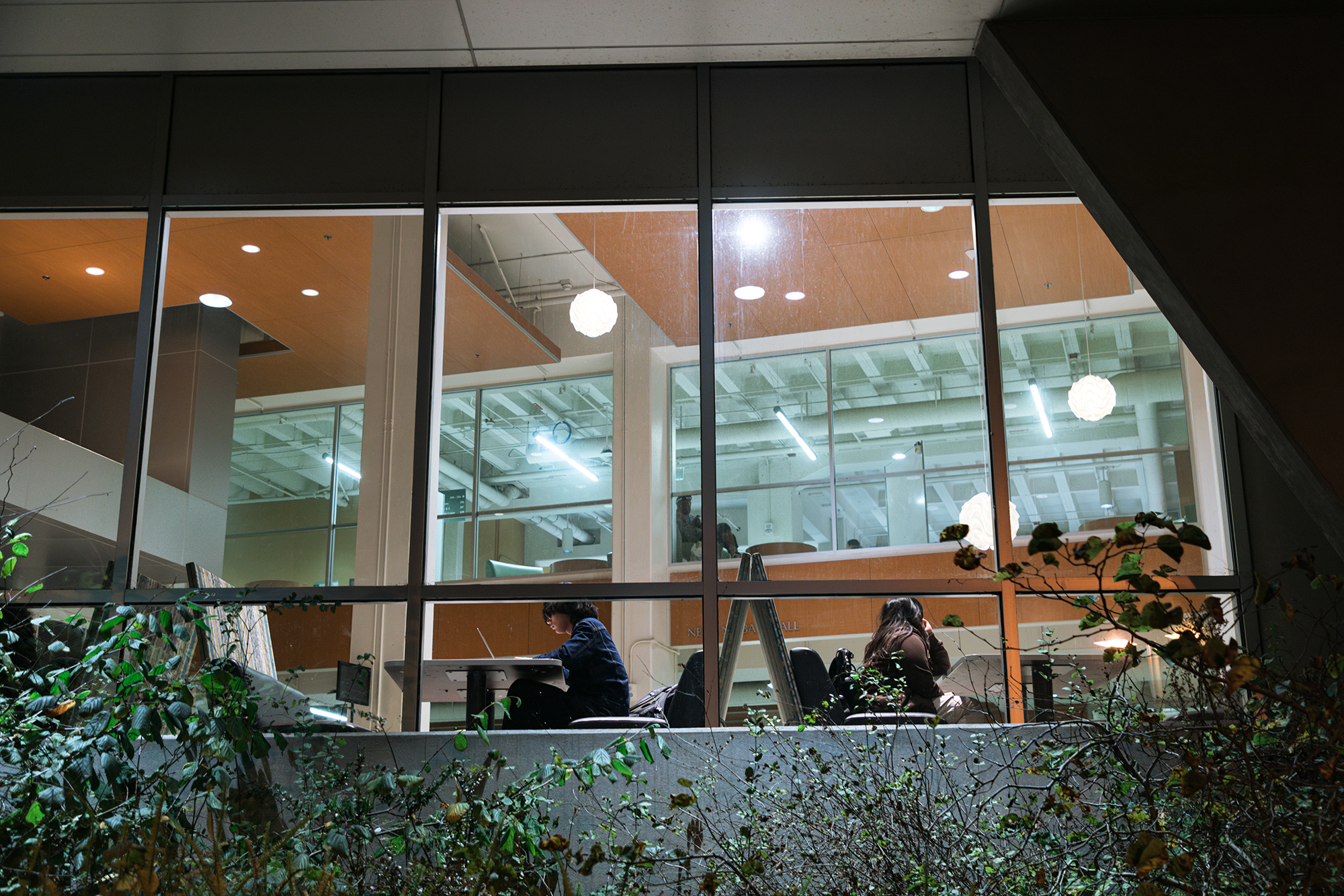 Outside shot of students working in the library at night.