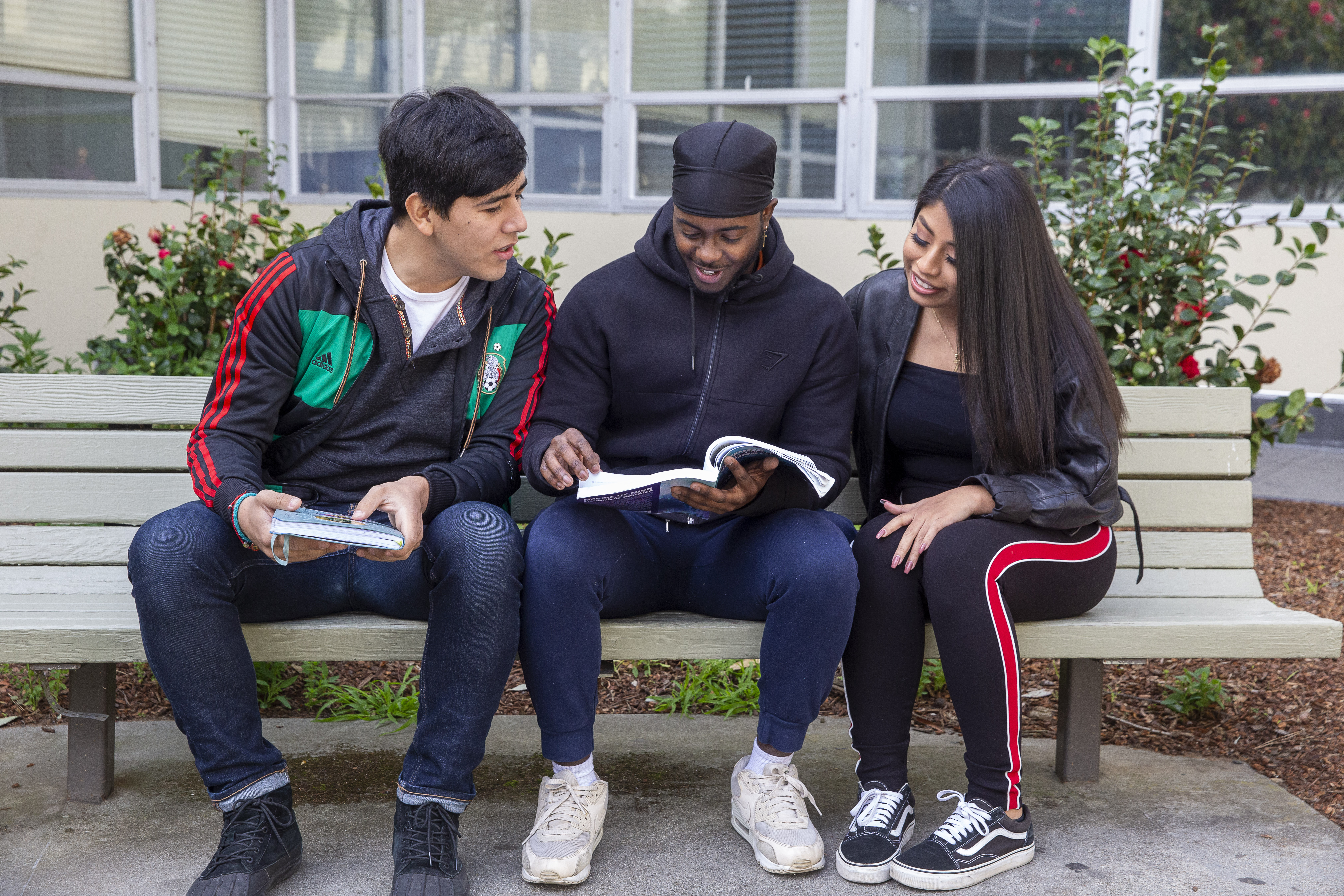 three students on bench looking at book